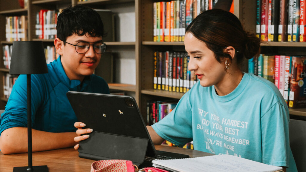 Two students working on a laptop in the library