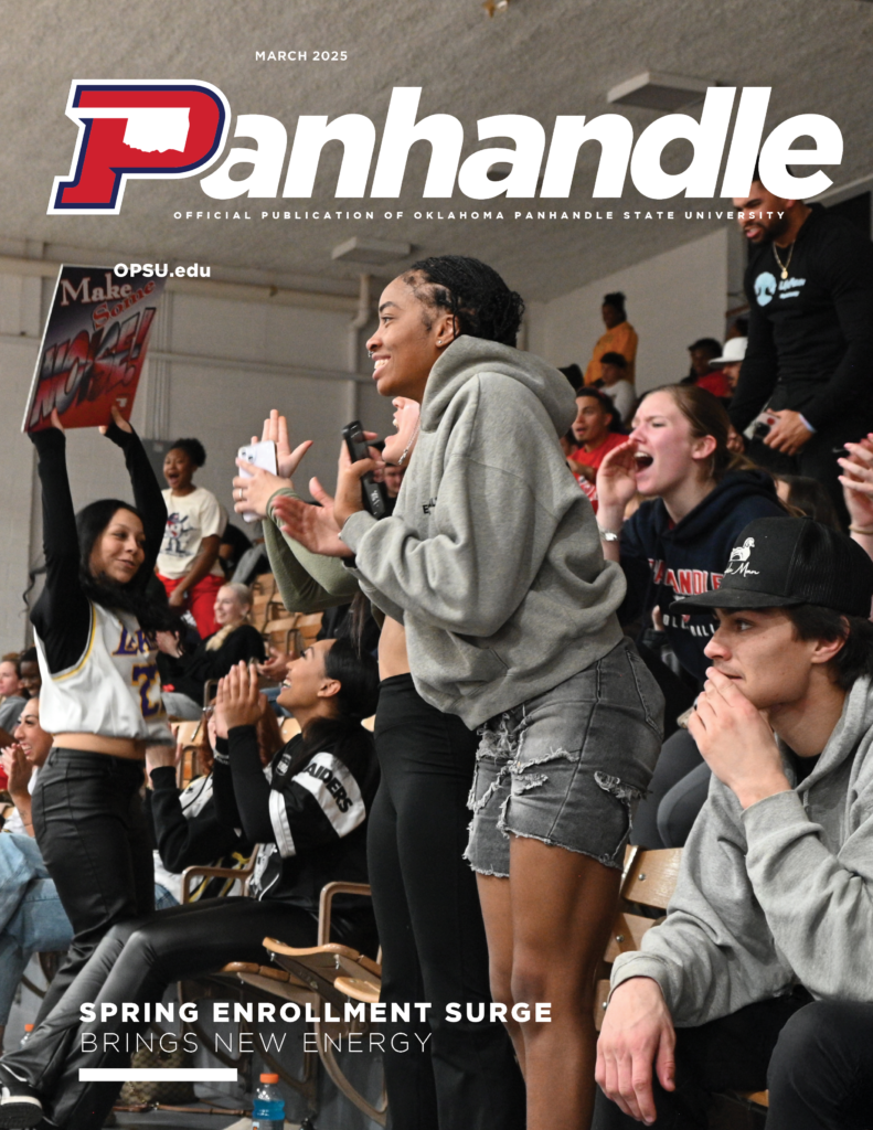 Several OPSU students standing and cheering at an Aggie Basketball game. 